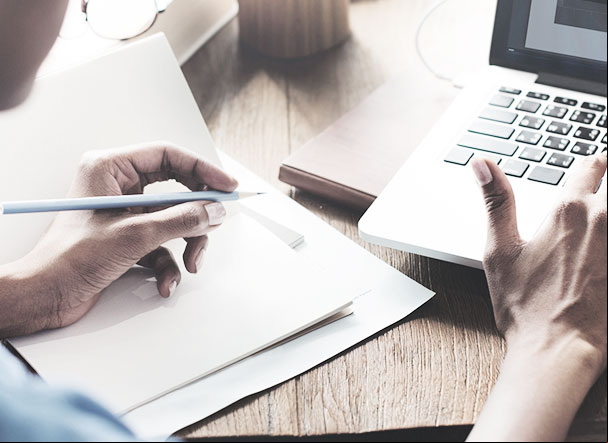 Person typing on notebook with right hand and writing on paper with left hand