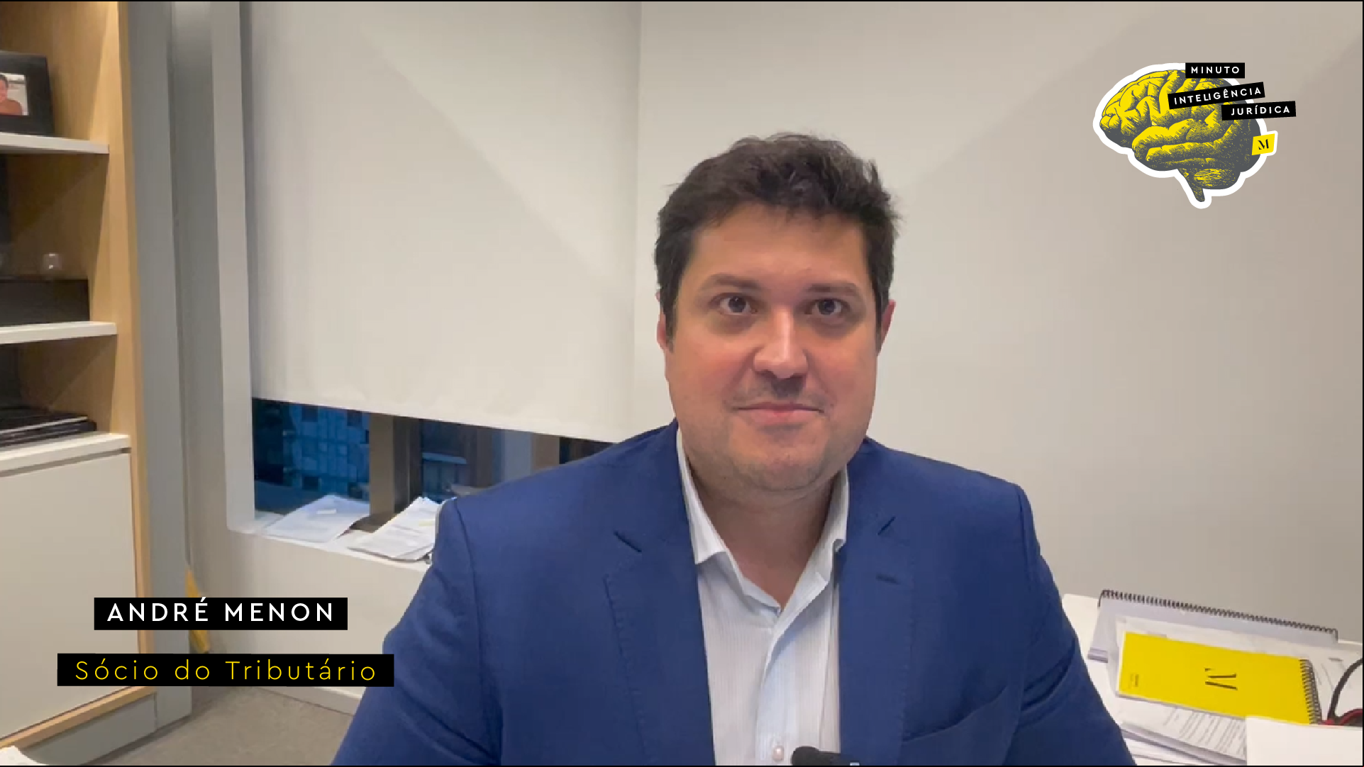 Homem olhando para a foto e sorrindo, usando terno azul marinho e camisa branca. No canto inferior esquerdo, frase com os dizeres "André Menon - sócio do Tributário". No canto superior direito, logotipo do Inteligência Jurídica