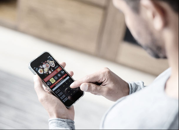 homem com camisa cinza e de costas para a imagem, mexendo no celular, em um site de apostas esportivas