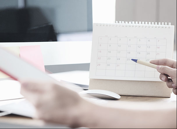 Person checking calendar while making notes in notepad