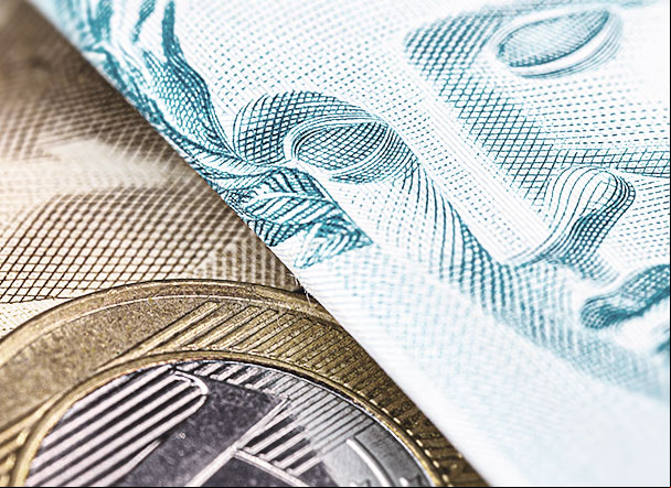 Nota de cem reais ao lado de moeda de um real