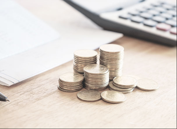 Pilhas de moedas em diferentes tamanhos na cor dourada. Ao fundo, calculadora cinza