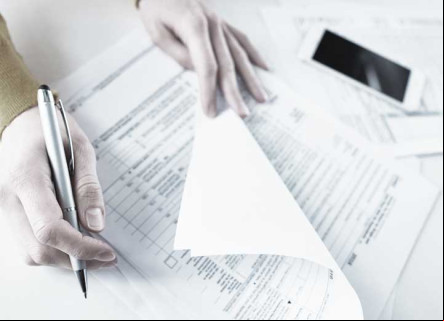 Top view of person holding pen in right hand and checking documents with right hand